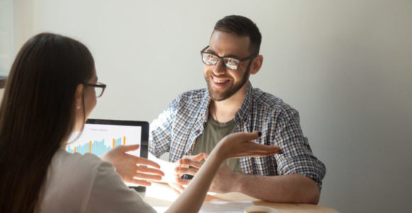 Two friendly businesspeople discussing contract details. Female agent explains contract, deal, loan details to smiling man. Coworkers negotiating, planning teamwork. Increasing charts on laptop screen